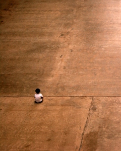 lone person sitting on large expanse of concrete