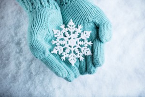 Female hands in light teal knitted mittens with sparkling wonderful snowflake 