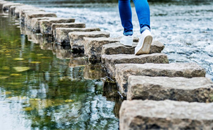 person walking across a stream on stepping stones